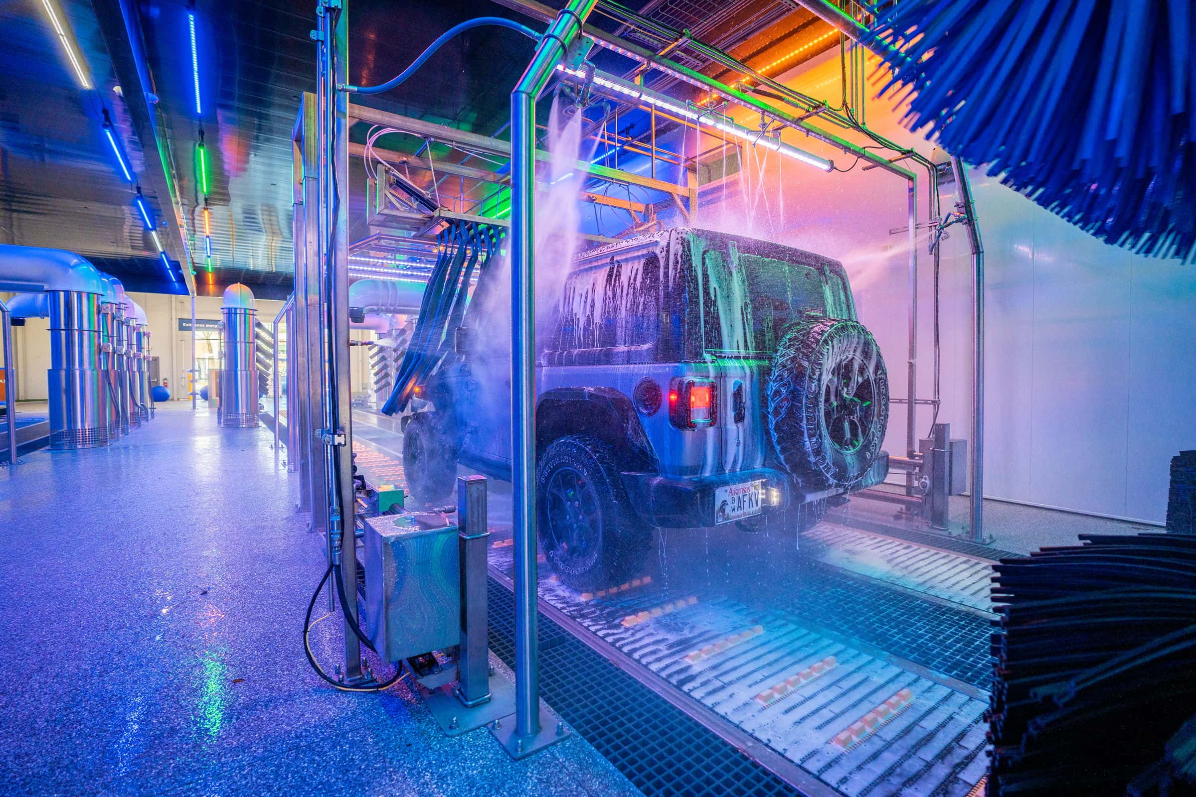A Jeep being washed in the Splash tunnel, foam sheeting off the body under neon arches